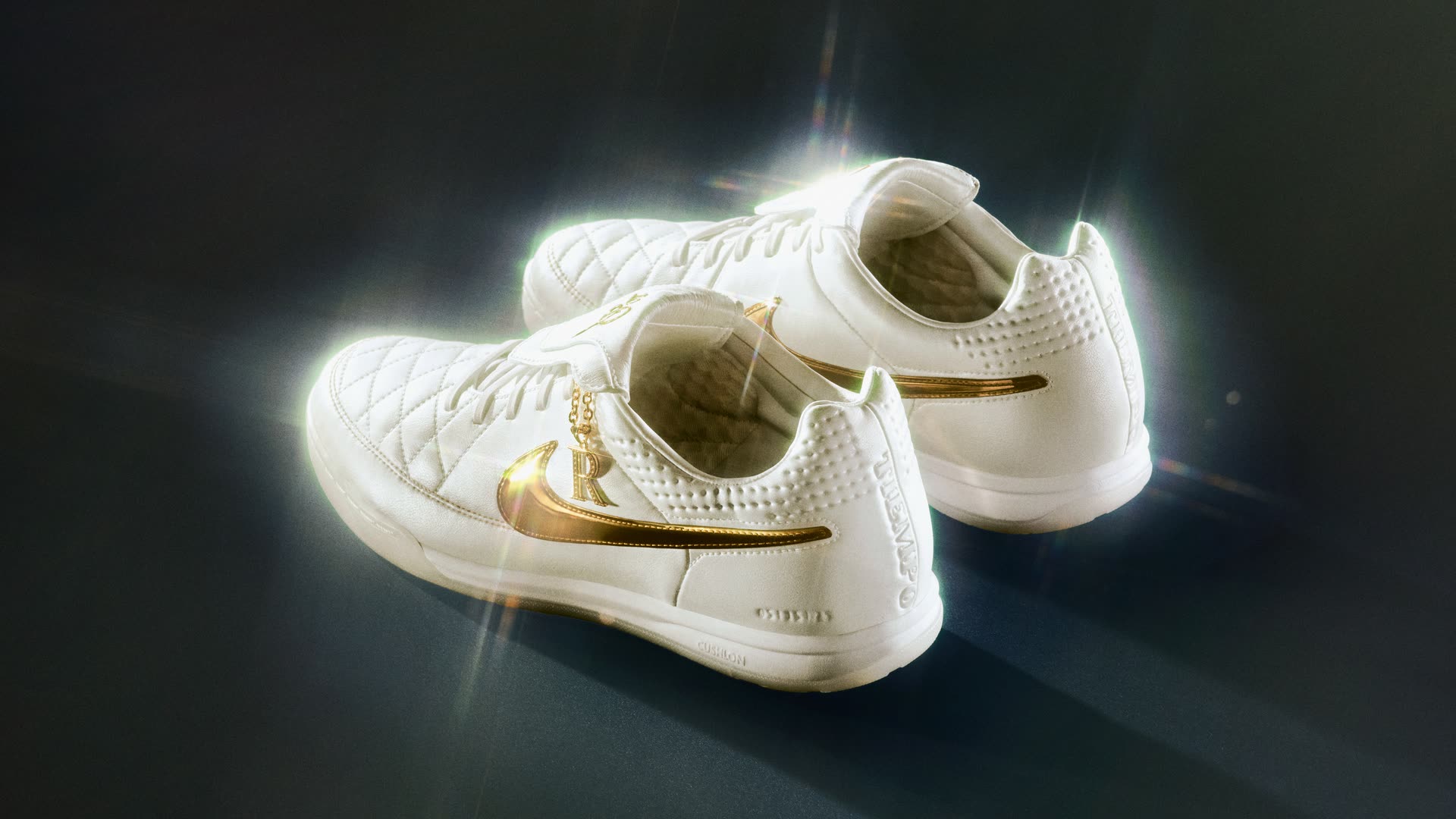 Пара білих зальних Nike Tiempo із золотим логотипом на темному тлі
